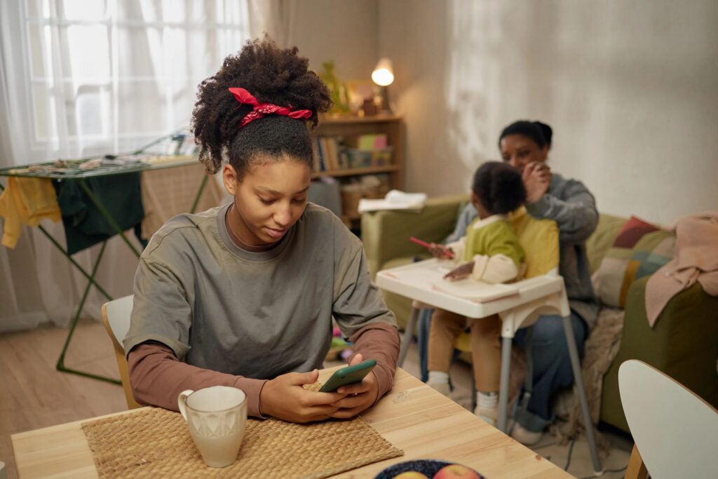 Black Teenage Girl Checking Smartphone While Family Managing Home Stress